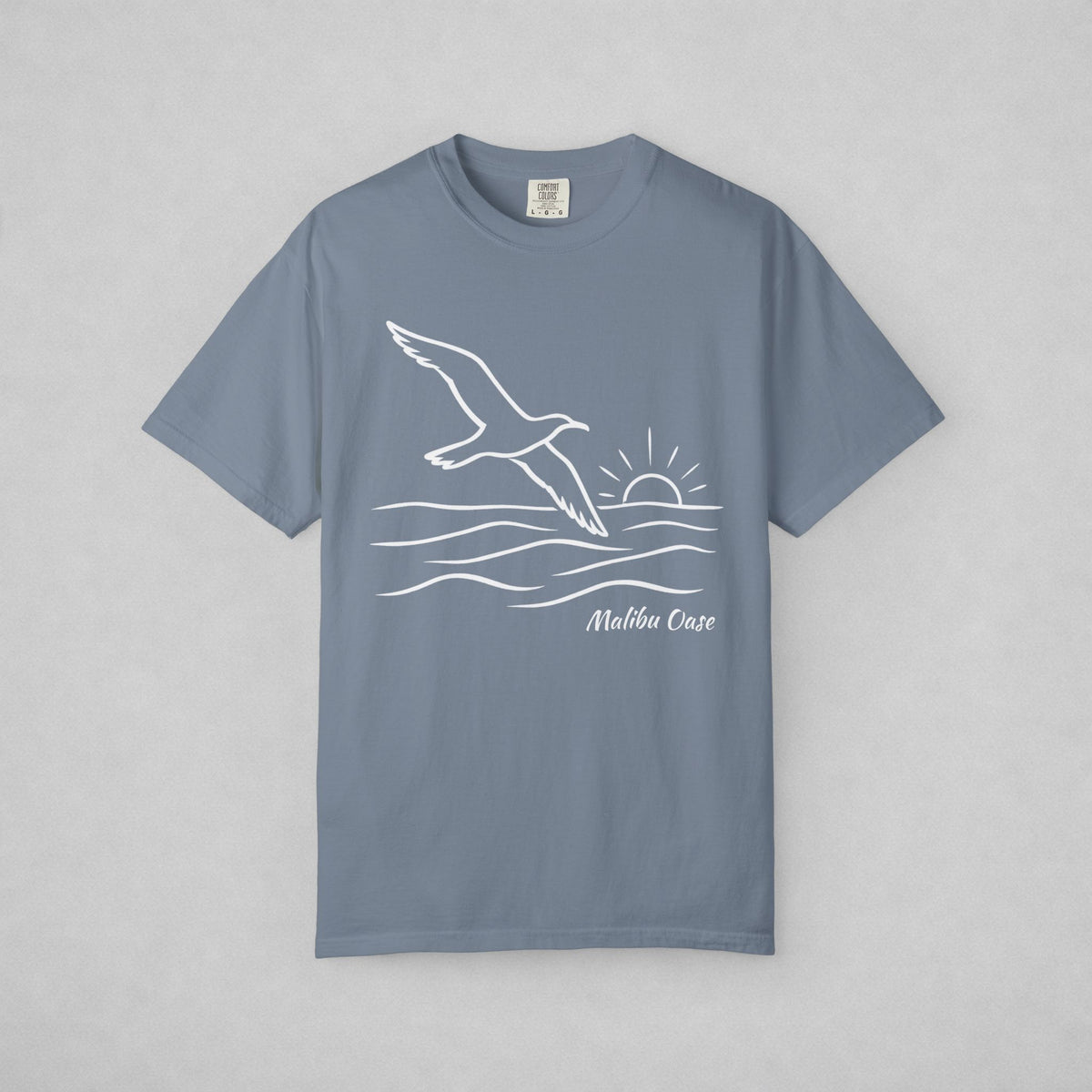 Blue Jean.  Short-sleeve t-shirt with a white line art graphic of a flying seagull, waves, a rising sun, and the text Malibu Oase' on the front, displayed flat against a neutral gray background.