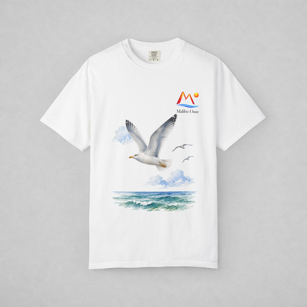 A white short-sleeve crewneck t-shirt featuring a watercolor-style graphic of a flying seagull over blue-green ocean waves, with a small 'Malibu Oase' logo on the upper right chest, displayed on a neutral gray background.