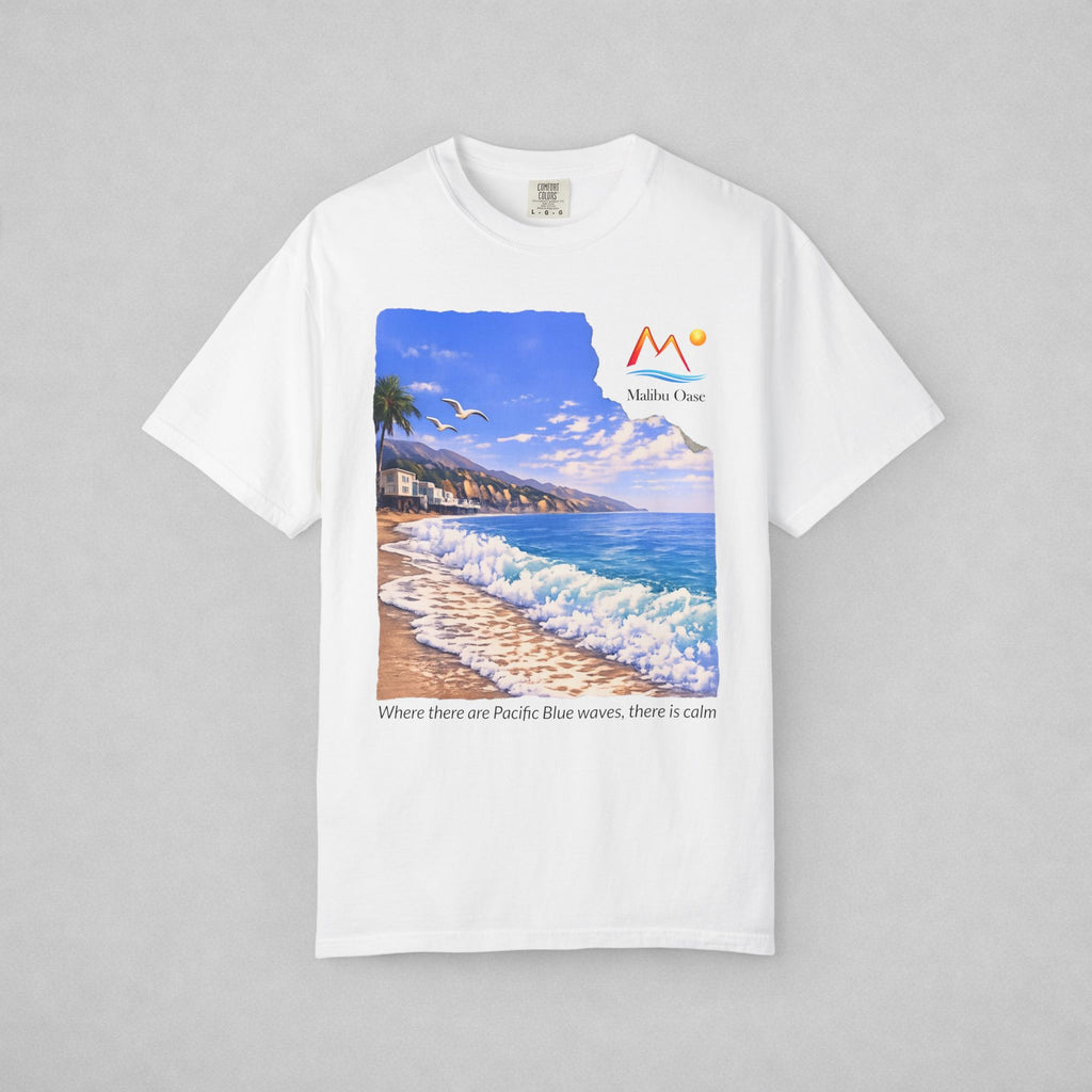A white short-sleeve crewneck t-shirt with a large graphic print of a beach scene on the front. The graphic features a blue sky, ocean waves, a sandy beach, and a palm tree, with the logo 'Malibu Oase' and under the print there are the words 'Where there are Pacific Blue waves, there is calm'.