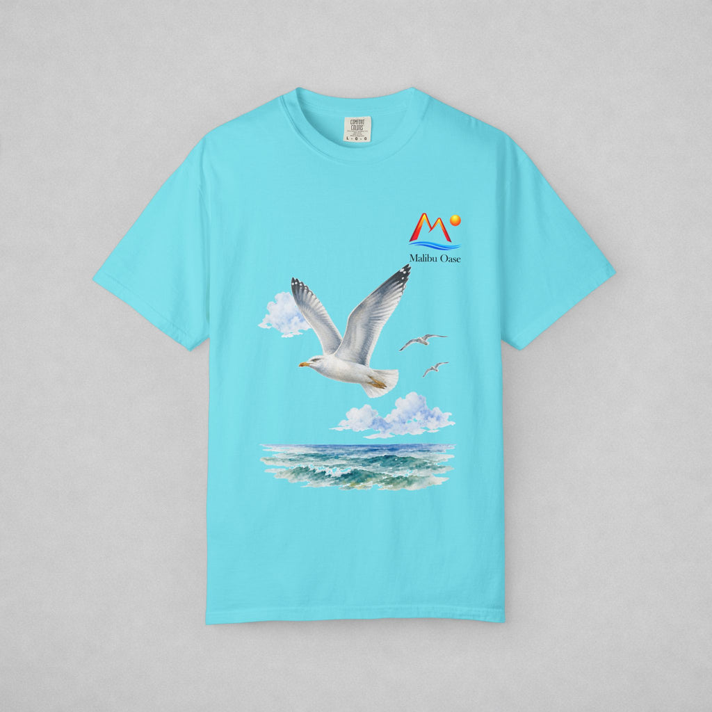 A light blue short-sleeve t-shirt with a graphic print of a seagull flying over ocean waves, accompanied by a 'Malibu Oase' logo on the chest, displayed on a neutral gray background.