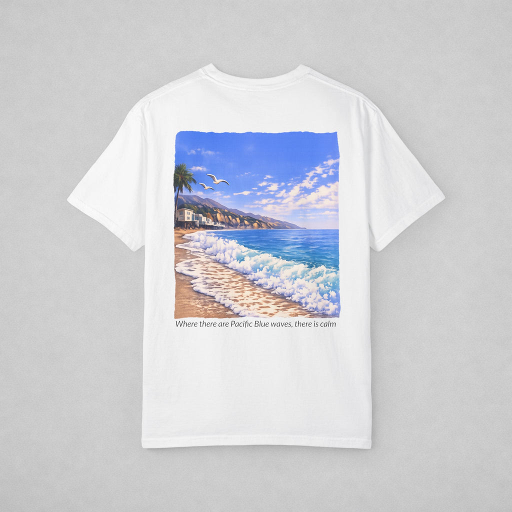 A white short-sleeve crewneck t-shirt with a square graphic print of a beach scene featuring blue ocean waves, a sandy shore, and a blue sky. Below the graphic, the text reads 'Where there are Pacific Blue waves, there is calm'.