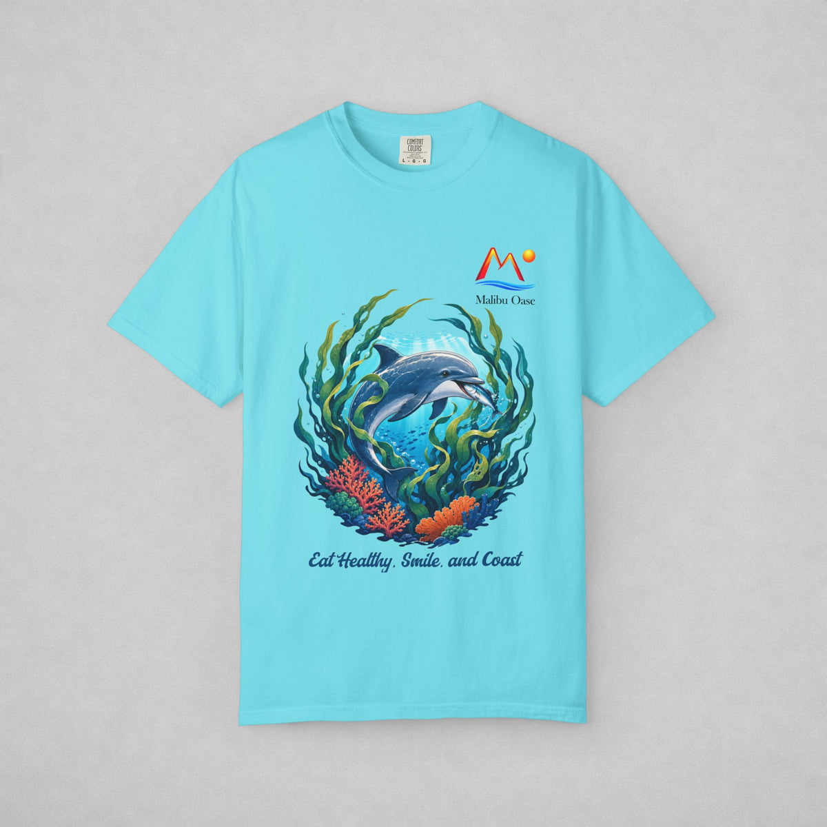 A light blue short-sleeve t-shirt with a central graphic of a dolphin swimming among green seaweed and orange coral, with the text 'Eat Healthy, Smile and Coast.'