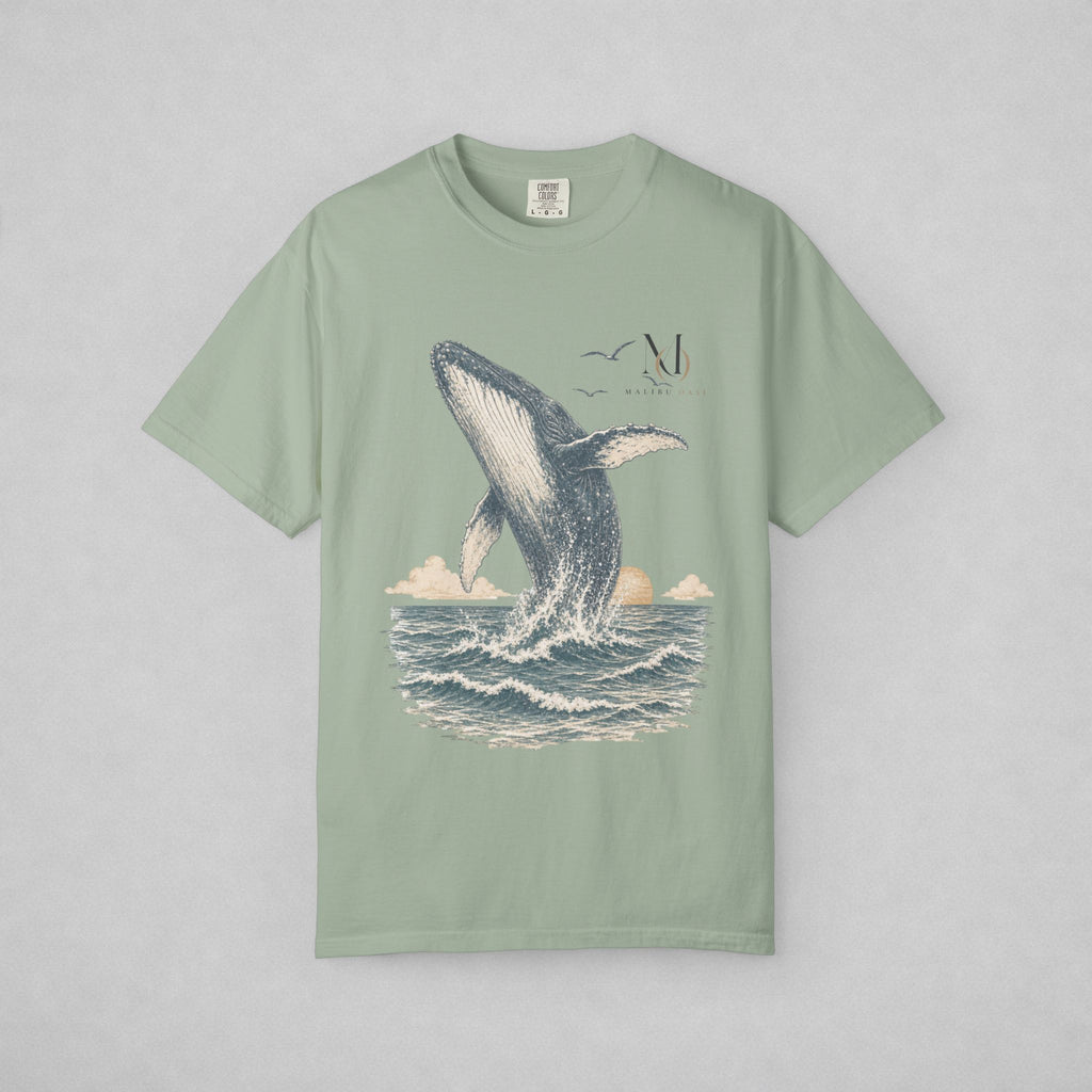 A sage green short-sleeve t-shirt with a graphic print of a whale jumping out of the ocean, displayed flat against a light gray background.
