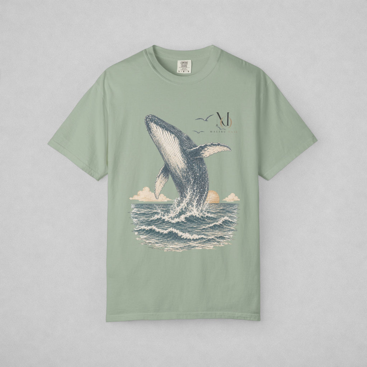 A sage green short-sleeve t-shirt with a graphic print of a whale jumping out of the ocean, displayed flat against a light gray background.