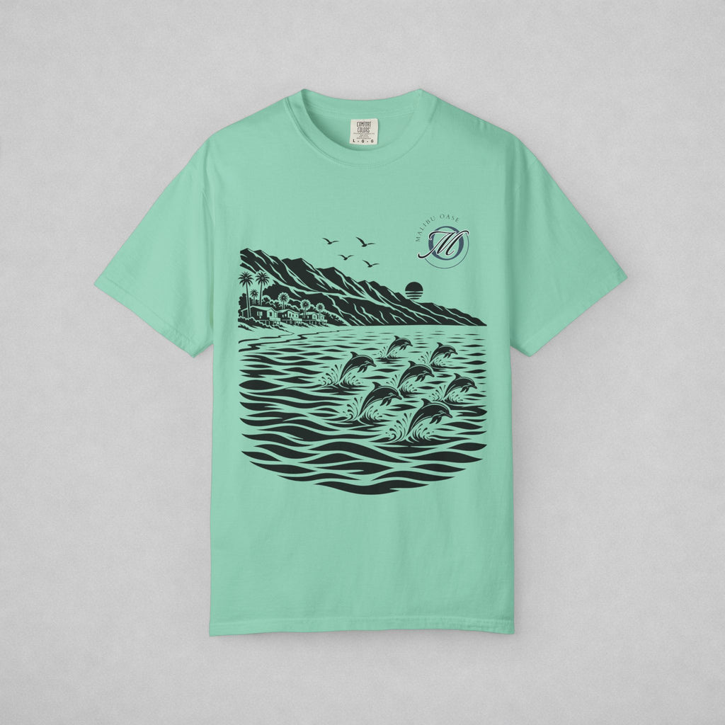 A mint green short-sleeve t-shirt with a black graphic print of dolphins jumping in water, mountains, and birds, displayed flat against a light gray background.