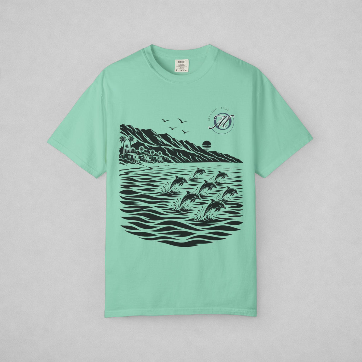 A mint green short-sleeve t-shirt with a black graphic print of dolphins jumping in water, mountains, and birds, displayed flat against a light gray background.