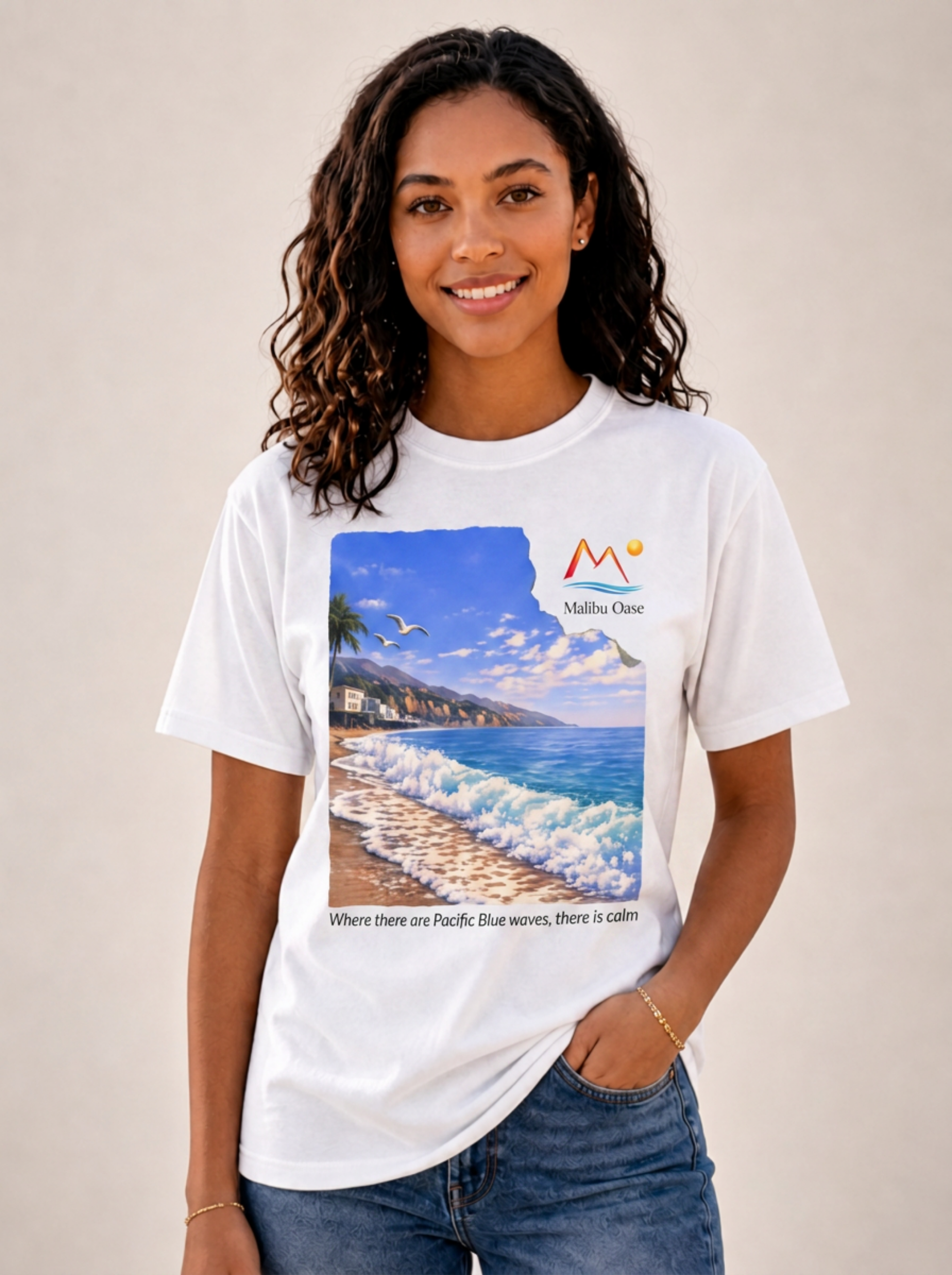 A woman wearing a white graphic t-shirt featuring a scenic print of a beach and ocean with the logo 'Malibu Oase' and 'Where there are Pacific Blue waves, there is calm'.