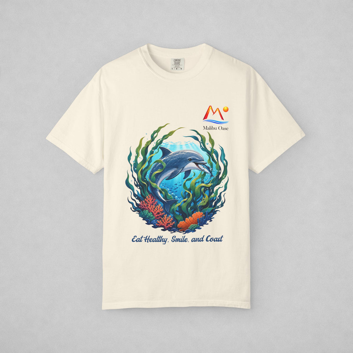 An off-white short-sleeve t-shirt with a colorful graphic of a dolphin swimming underwater with green seaweed and coral. The graphic includes the text 'Eat Healthy, Smile and Coast.'