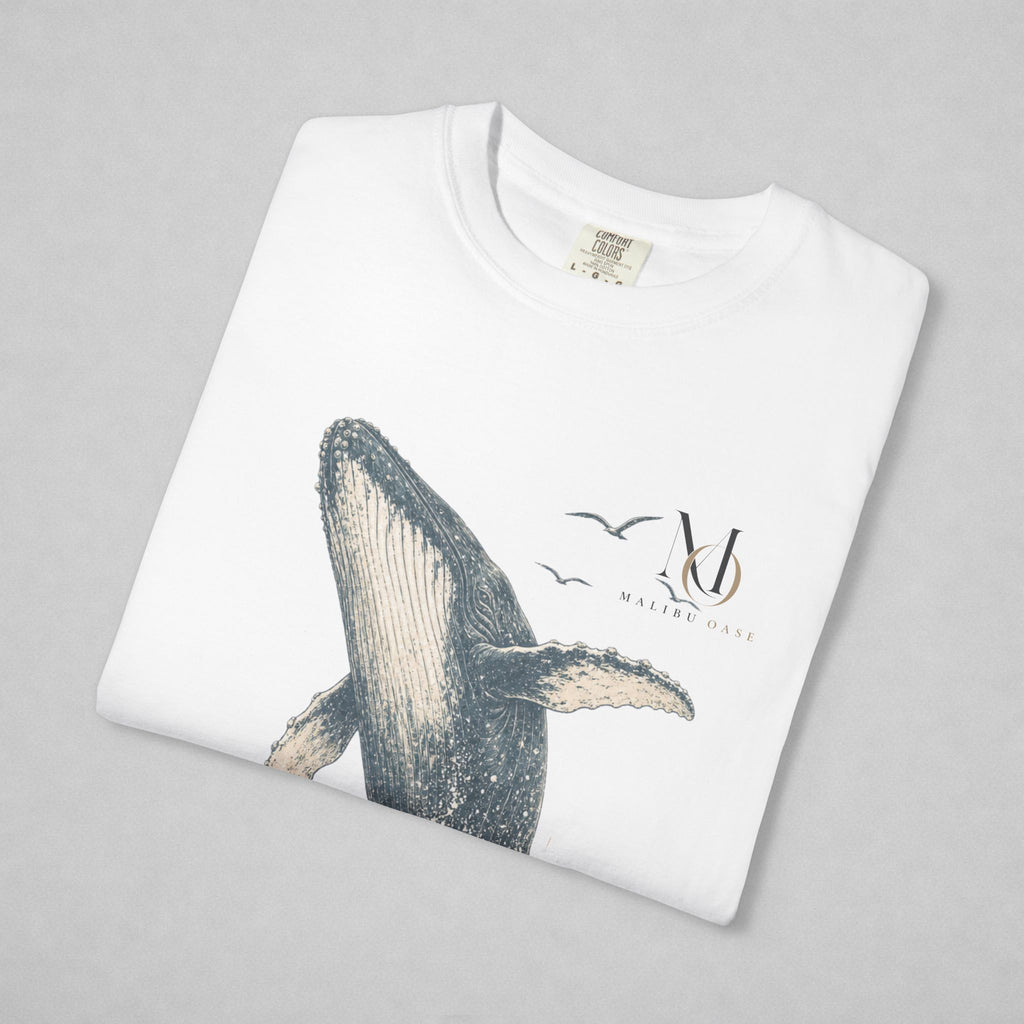A folded white crewneck sweatshirt on a light gray background, featuring a graphic print of a whale, birds, and a stylized 'Malibu Oase' monogram.