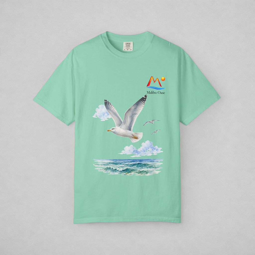 A mint green short-sleeve t-shirt with a graphic print of a flying seagull over blue ocean waves under white clouds, featuring a 'Malibu Oase' logo on the chest, displayed flat against a light gray background.