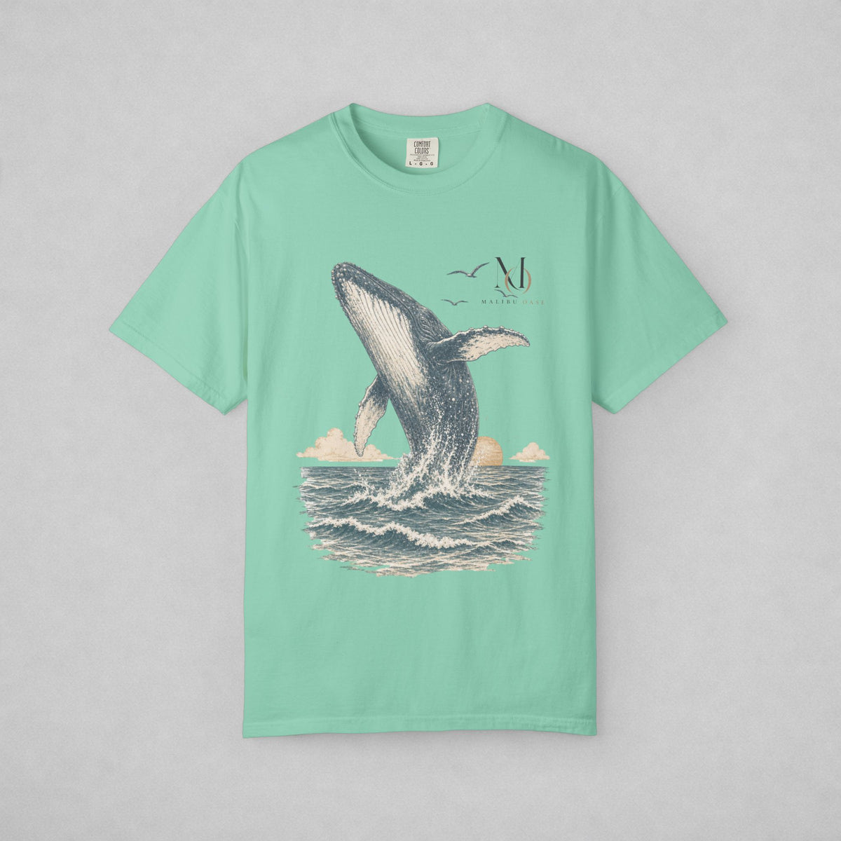 A mint green short-sleeve t-shirt with a graphic print of a whale jumping out of the ocean, shown flat against a neutral gray background.