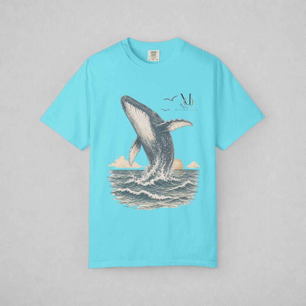 A light blue short-sleeve crewneck t-shirt featuring a detailed graphic print of a humpback whale breaching the ocean, with small birds in the sky. The shirt is displayed flat against a neutral gray background.