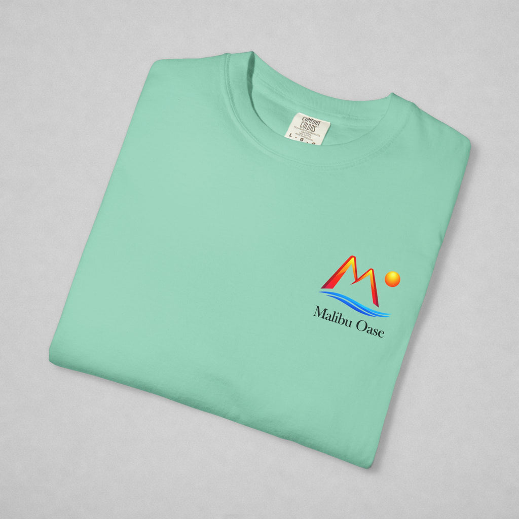 A folded mint green t-shirt with a colorful 'Malibu Oase' graphic on the left chest, displayed on a neutral gray background.