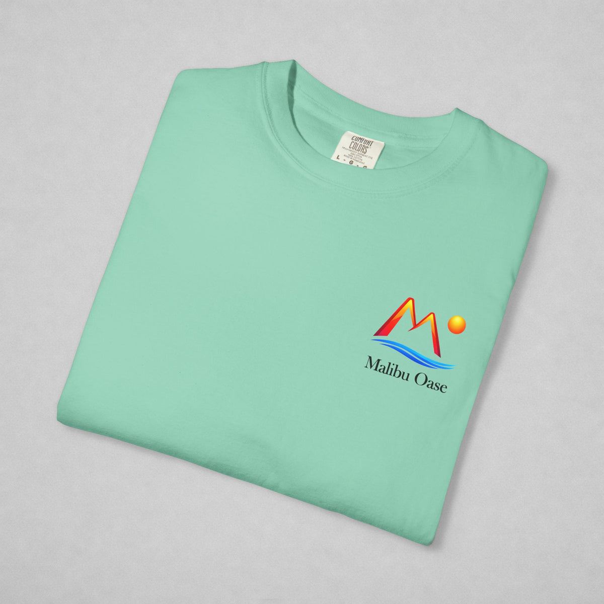 A folded mint green t-shirt with a colorful 'Malibu Oase' graphic on the left chest, displayed on a neutral gray background.