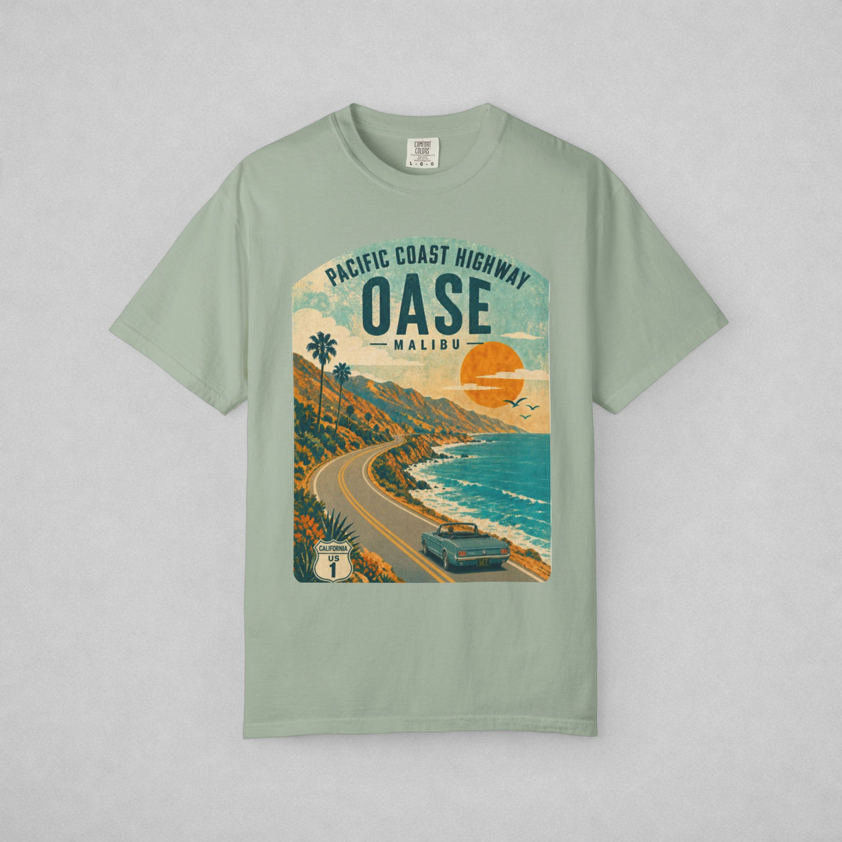 A sage green short-sleeve t-shirt with a vintage-style graphic print of the Pacific Coast Highway Oase Malibu, featuring a retro car, palm trees, and a sunset over the ocean.