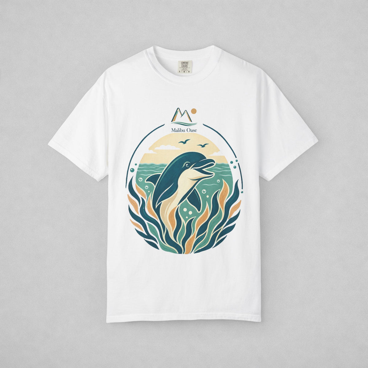 A white short-sleeve crewneck t-shirt with a circular graphic print of a dolphin jumping from teal water with stylized waves and the text 'Maibu Oase', displayed flat against a neutral gray background.