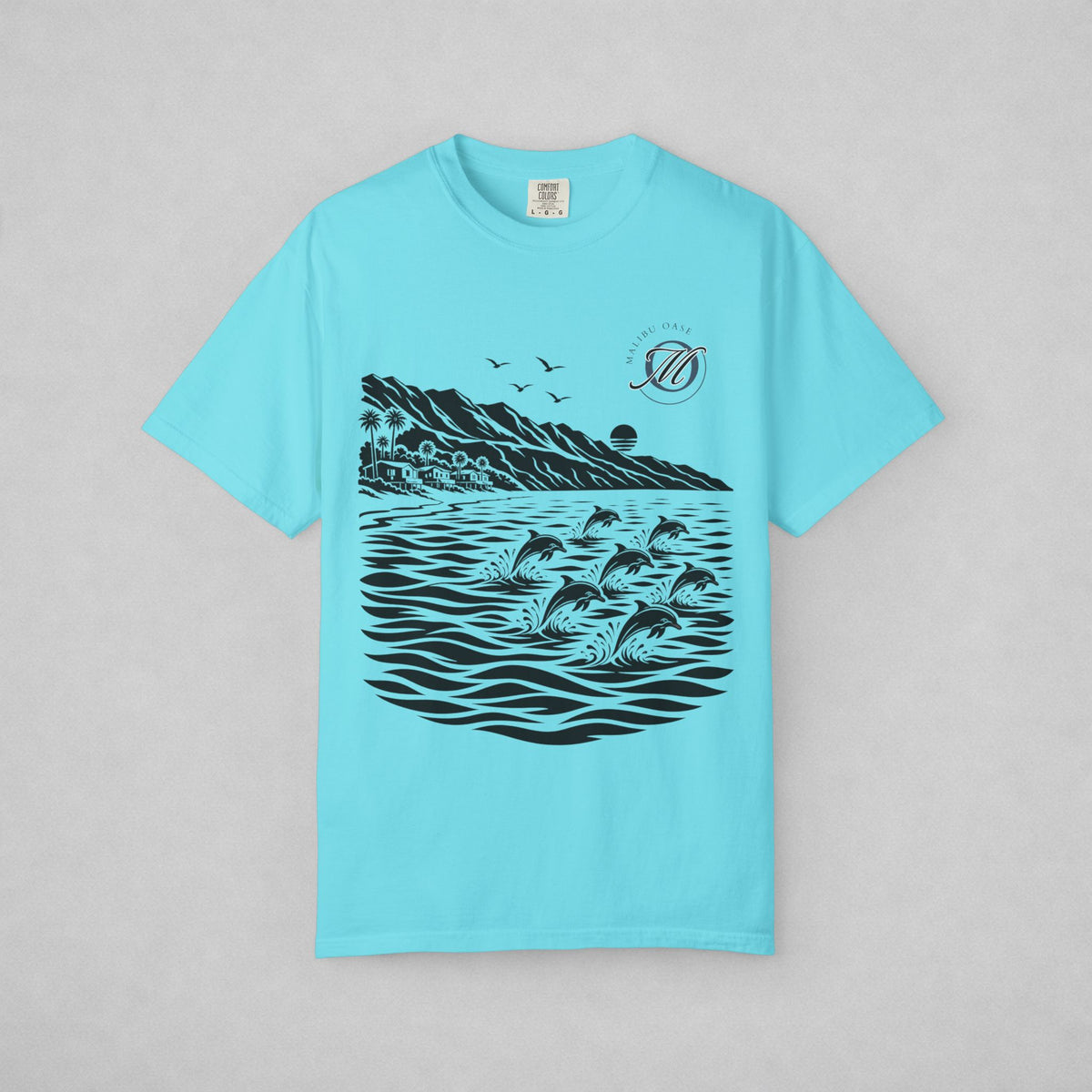 A light blue short-sleeve t-shirt with a black graphic print of dolphins jumping in the water, mountains, birds, and a sunset. The shirt is displayed flat against a neutral gray background.