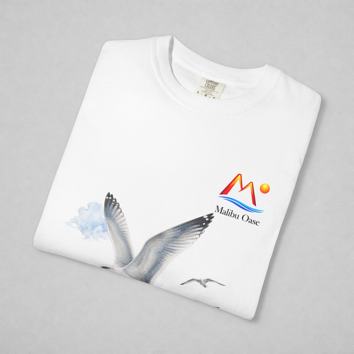 A folded white crewneck sweatshirt on a light gray background, featuring a graphic print of a flying seagull and a colorful 'Malibu Oase' logo on the left chest.