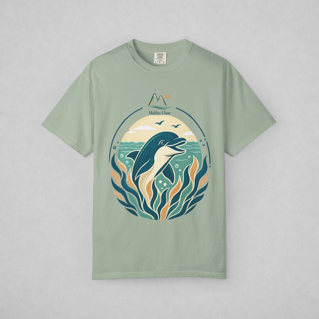 A sage green short-sleeve t-shirt with a circular graphic of a dolphin, waves, and stylized mountains, displayed flat against a light gray background.