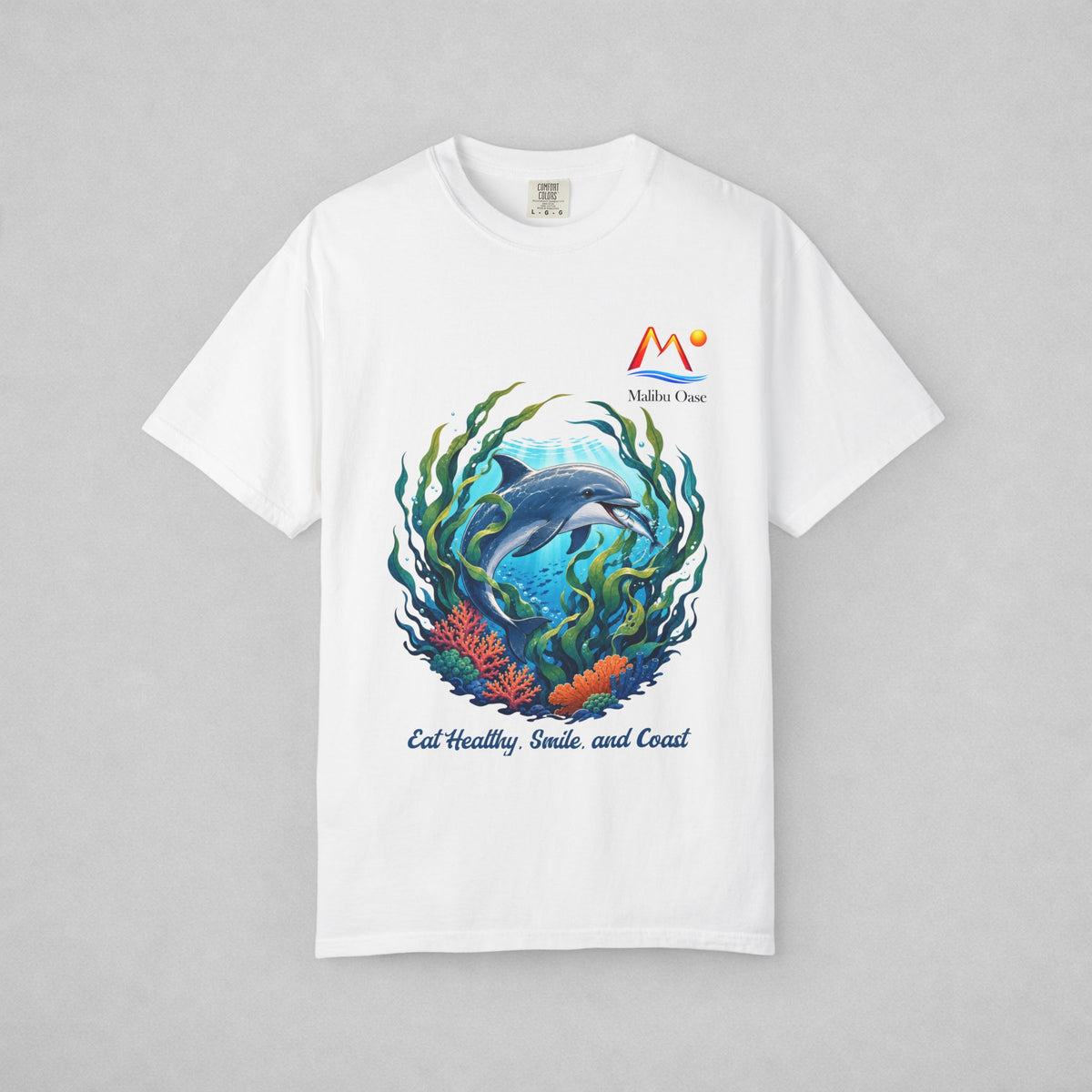 A white short-sleeve crewneck t-shirt with a colorful graphic of a dolphin swimming underwater with coral and seaweed, featuring the text 'Eat Healthy, Smile, and Coast' and a 'Malibu Oase' logo on the chest, displayed on a neutral gray background.